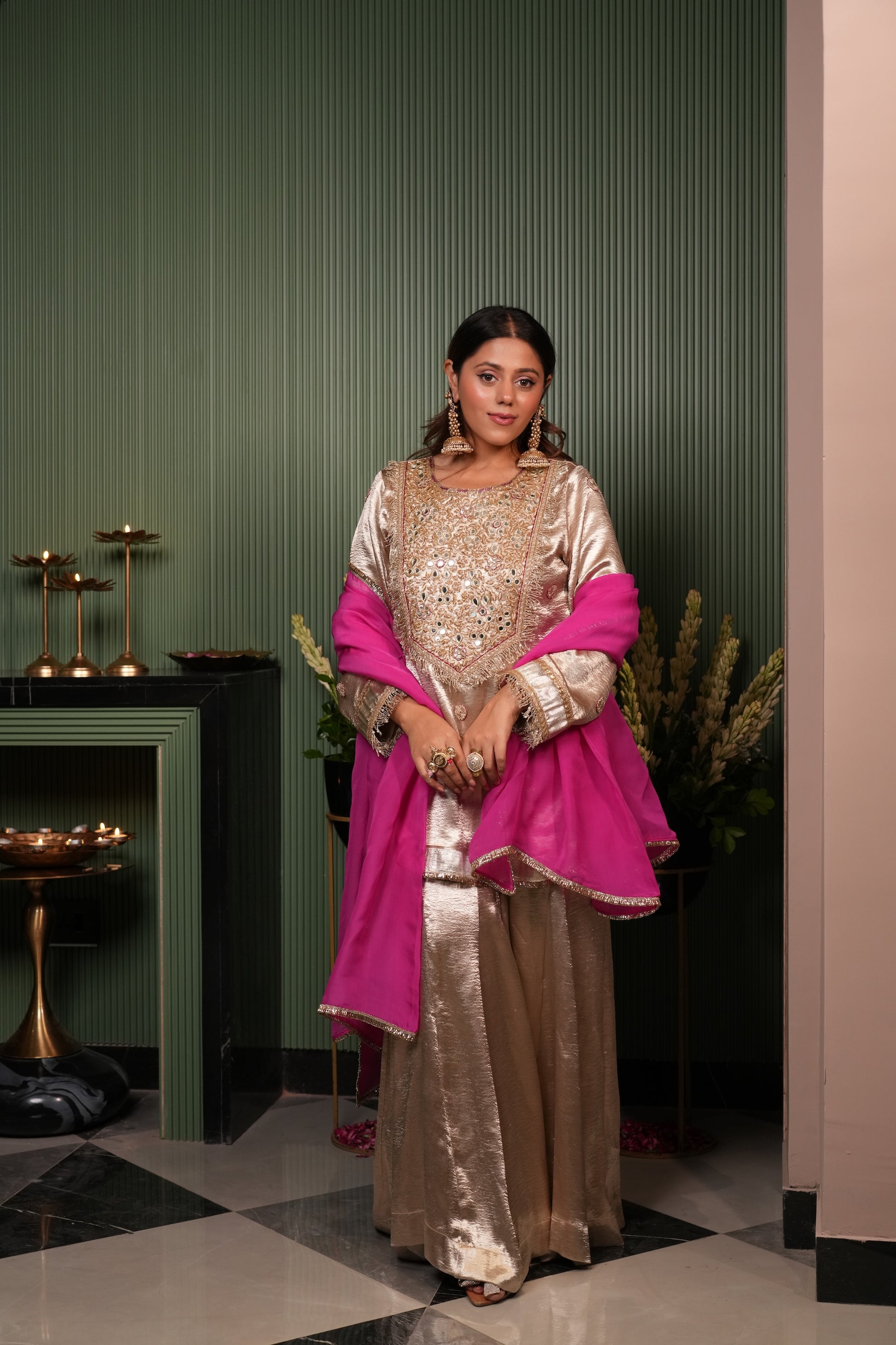 Woman in a gold and pink traditional outfit standing in a room with green walls and decorative elements.