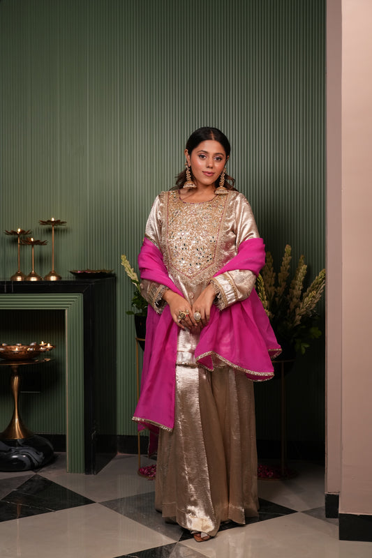 Woman in a gold and pink traditional outfit standing in a room with green walls and decorative elements.