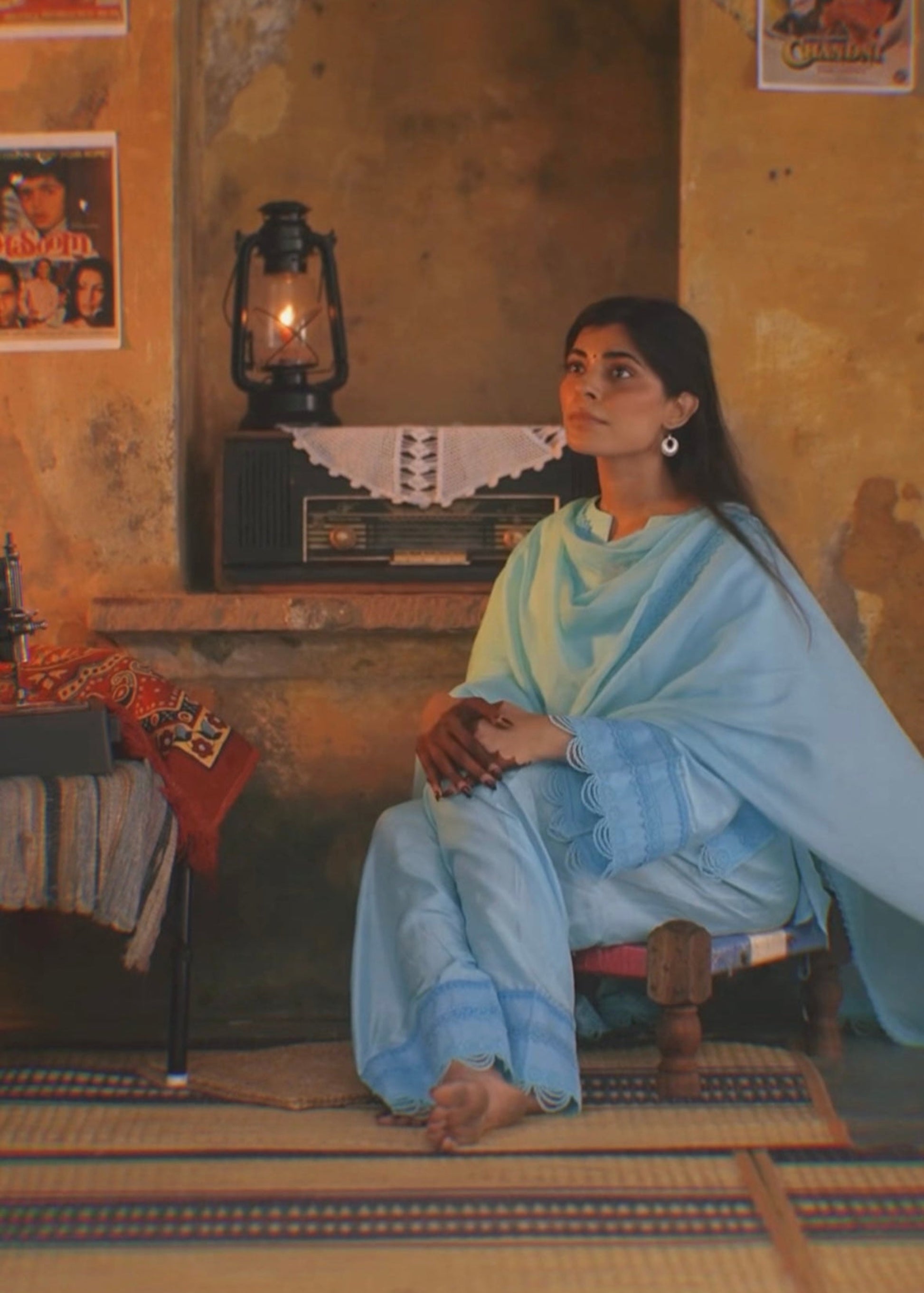 Woman in a blue sari sitting in a room with posters on the wall.